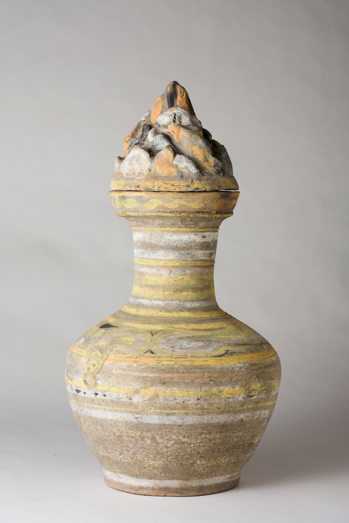 Han Dynasty earthenware pottery jar with mountain-shaped cover, painted yellow, white and black bands, and circular motifs.