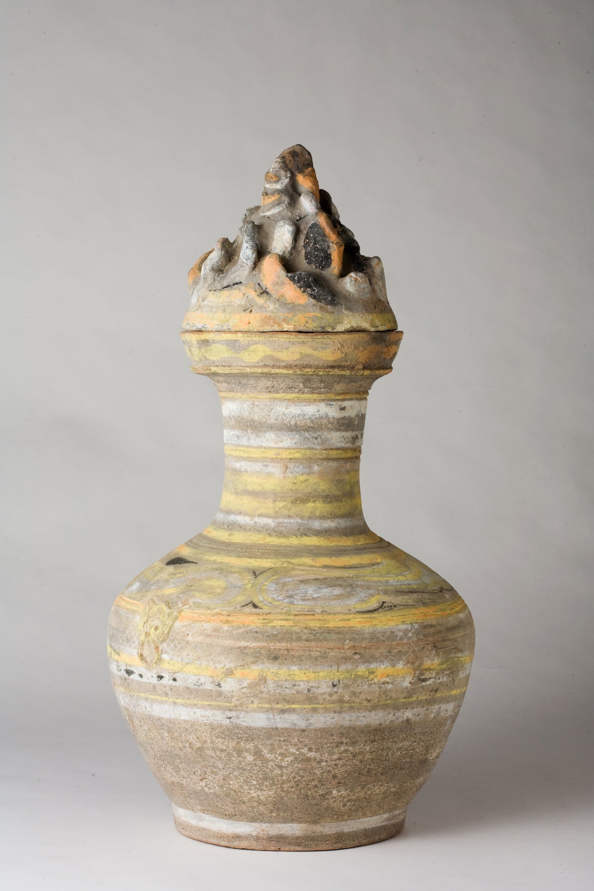 Han Dynasty earthenware pottery jar with mountain-shaped cover, painted yellow, white and black bands, and circular motifs.