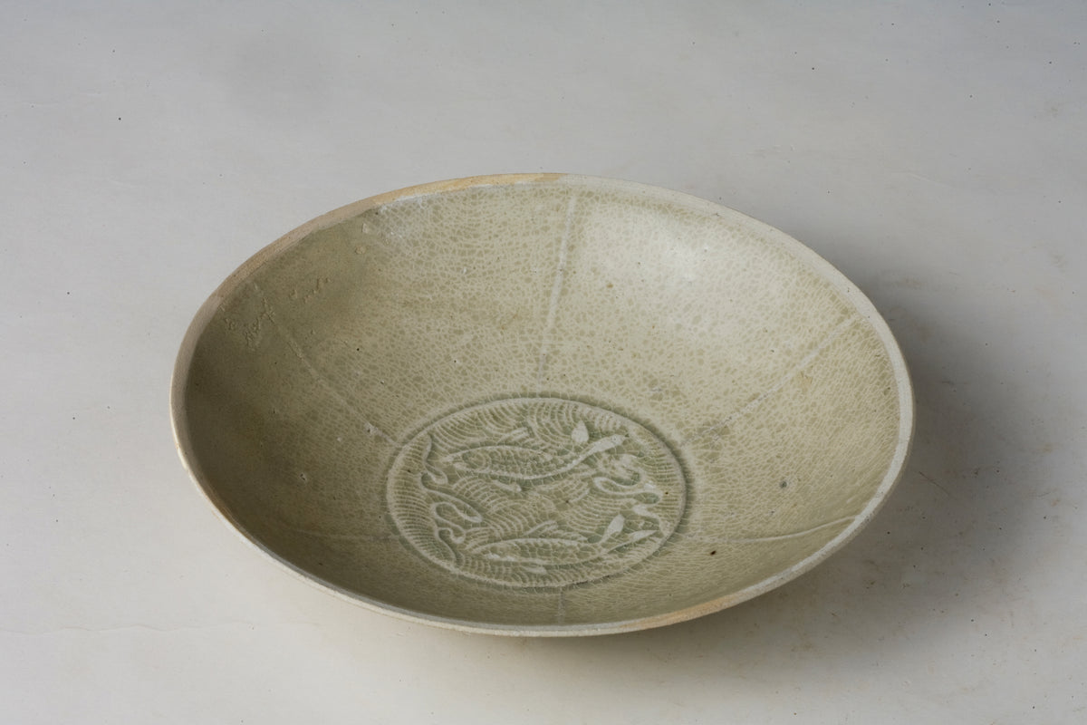 Song Dynasty porcelain bowl with carved twin-fish design, pale blue-white glaze, and low foot.